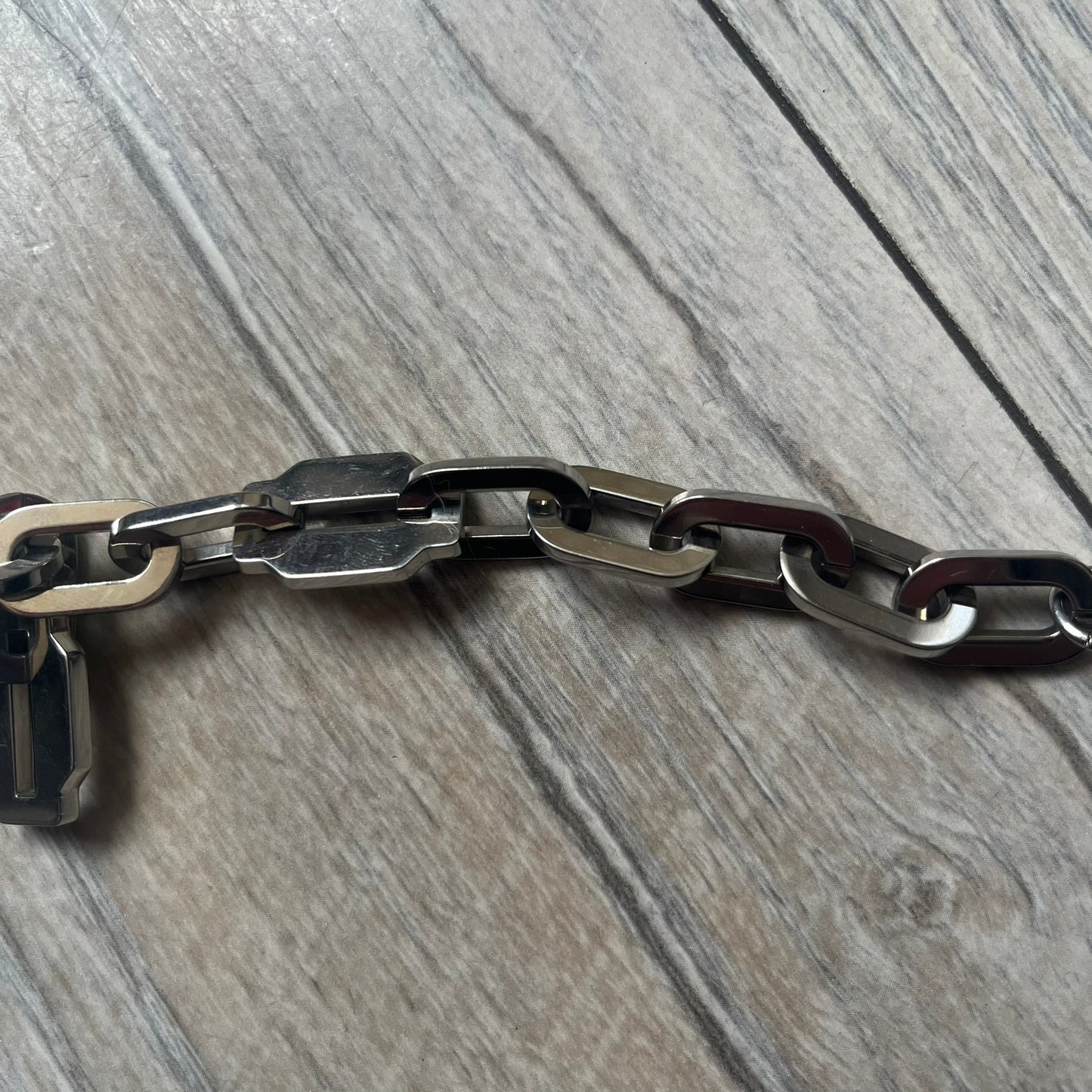 Dolce &amp; Gabbana Razorblade Sample Bracelet is a stainless steel chain bracelet with large interlocking links and a central razor blade-shaped pendant matching the link size. One side of the pendant is engraved with the D&amp;G logo, while the opposite side features small “SAMPLE” text. The bracelet secures with a lobster clasp engraved with Dolce &amp; Gabbana logos.
