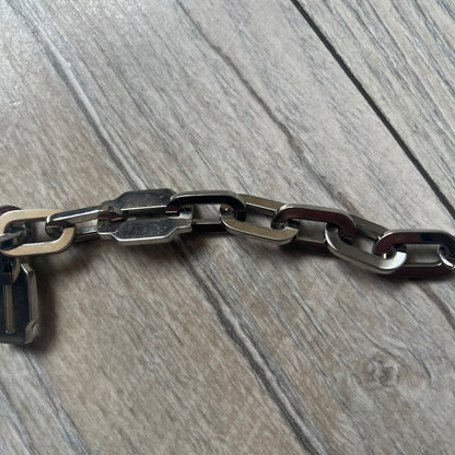 Dolce &amp; Gabbana Razorblade Sample Bracelet is a stainless steel chain bracelet with large interlocking links and a central razor blade-shaped pendant matching the link size. One side of the pendant is engraved with the D&amp;G logo, while the opposite side features small “SAMPLE” text. The bracelet secures with a lobster clasp engraved with Dolce &amp; Gabbana logos.