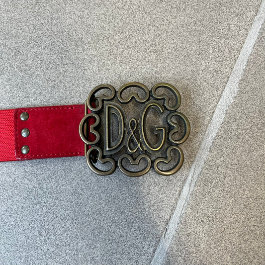 Dolce &amp; Gabbana Red Elastic Hearts Belt is made from red elastic material. The buckle is a metal D&amp;G logo surrounded by eight heart shapes pointing outward, all finished in a dark, aged-looking metal tone. The belt comes with the original hologram tag attached.