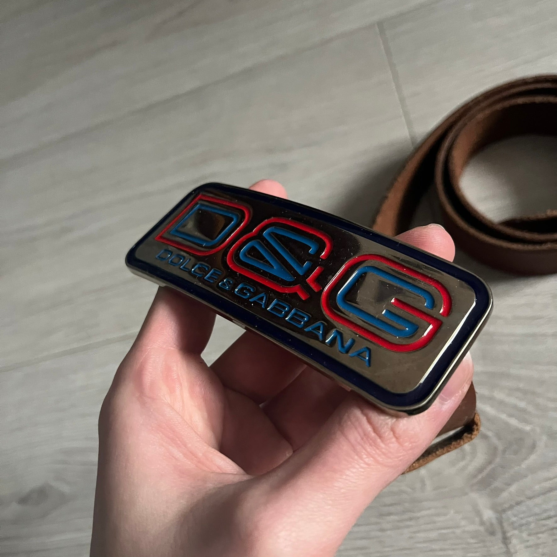 Dolce &amp; Gabbana Red &amp; Blue Leather Belt featuring a rectangular silver-tone buckle with a navy border. The buckle displays a large D&amp;G logo in blue with a red outline and “Dolce &amp; Gabbana” text in blue beneath. Finished with a brown leather strap.