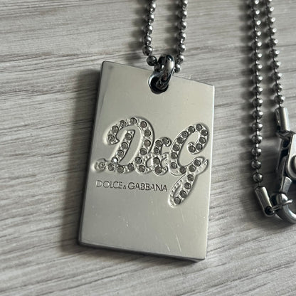 Dolce & Gabbana Rhinestones Dog Tag Necklace DJ0704 crafted from polished stainless steel. Features a rectangular pendant with the iconic D&G logo detailed in rhinestones, and “Dolce & Gabbana” engraved subtly below. Secured with a lobster clasp and finished with a durable ball chain.
