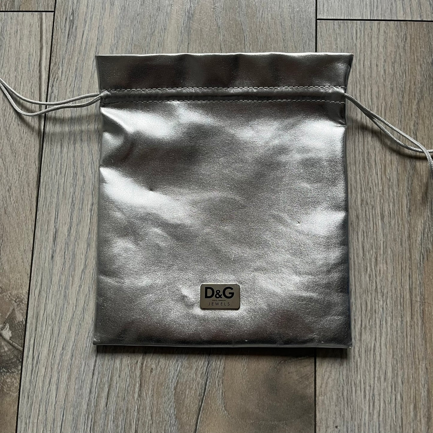 The Dolce &amp; Gabbana Room 13 Carabiner Necklace (DJ0613) is a large, heavy silver-tone necklace featuring a thick paperclip chain with oversized links. At the end of the chain is a large lobster clasp engraved with D&amp;G markings, connected to a branded carabiner. Hanging from the carabiner are two different keys with small D&amp;G logos and a black key identifier with a silver-tone plate engraved with “D&amp;G Dolce &amp; Gabbana Room 13.” The necklace comes with a large silver Dolce &amp; Gabbana dus