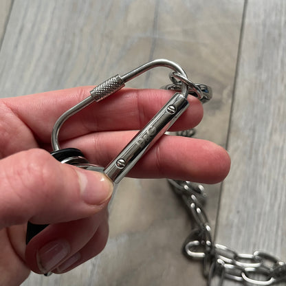 The Dolce &amp; Gabbana Room 13 Carabiner Necklace (DJ0613) is a large, heavy silver-tone necklace featuring a thick paperclip chain with oversized links. At the end of the chain is a large lobster clasp engraved with D&amp;G markings, connected to a branded carabiner. Hanging from the carabiner are two different keys with small D&amp;G logos and a black key identifier with a silver-tone plate engraved with “D&amp;G Dolce &amp; Gabbana Room 13.” The necklace comes with a large silver Dolce &amp; Gabbana dus
