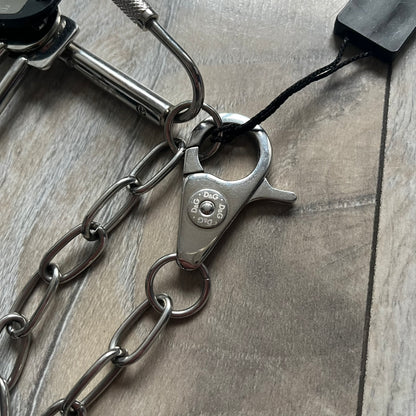 The Dolce &amp; Gabbana Room 13 Carabiner Necklace (DJ0613) is a large, heavy silver-tone necklace featuring a thick paperclip chain with oversized links. At the end of the chain is a large lobster clasp engraved with D&amp;G markings, connected to a branded carabiner. Hanging from the carabiner are two different keys with small D&amp;G logos and a black key identifier with a silver-tone plate engraved with “D&amp;G Dolce &amp; Gabbana Room 13.” The necklace comes with a large silver Dolce &amp; Gabbana dus