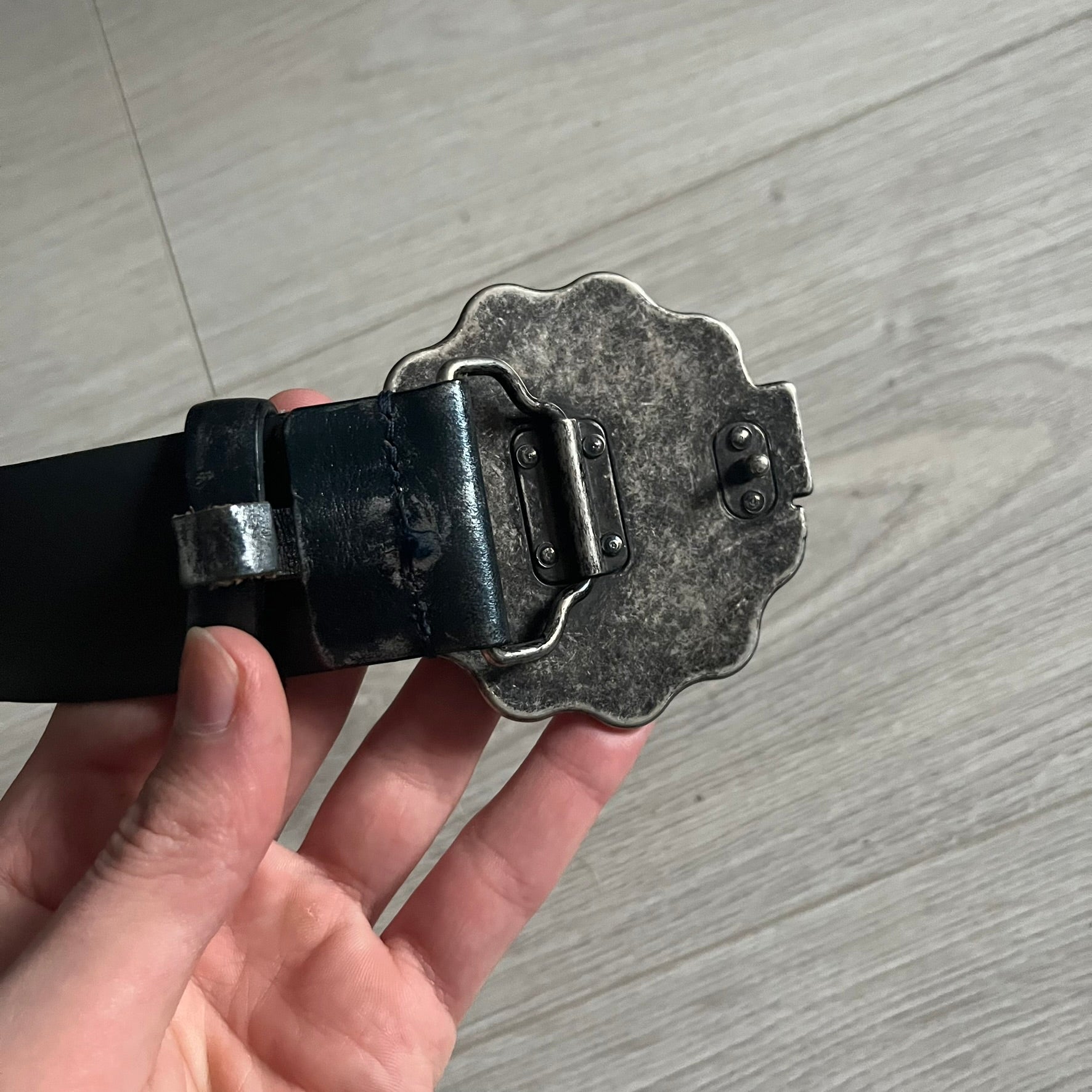 Dolce &amp; Gabbana Round Stamp Belt with a circular, wavy-edged buckle in a metallic finish. The buckle features a beige center with a bold black D&amp;G logo and “Dolce &amp; Gabbana” text beneath. Belt strap is glittery metallic blue with a black inner lining.