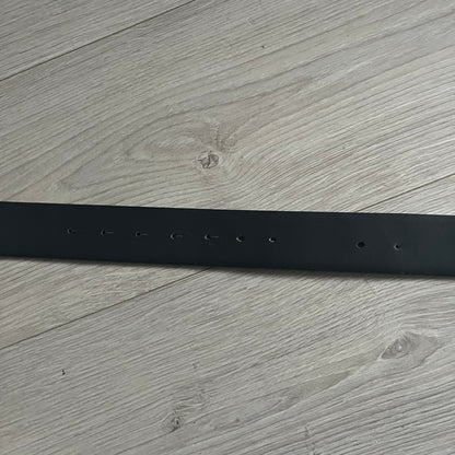 Dolce &amp; Gabbana Round Stamp Belt with a circular, wavy-edged buckle in a metallic finish. The buckle features a beige center with a bold black D&amp;G logo and “Dolce &amp; Gabbana” text beneath. Belt strap is glittery metallic blue with a black inner lining.