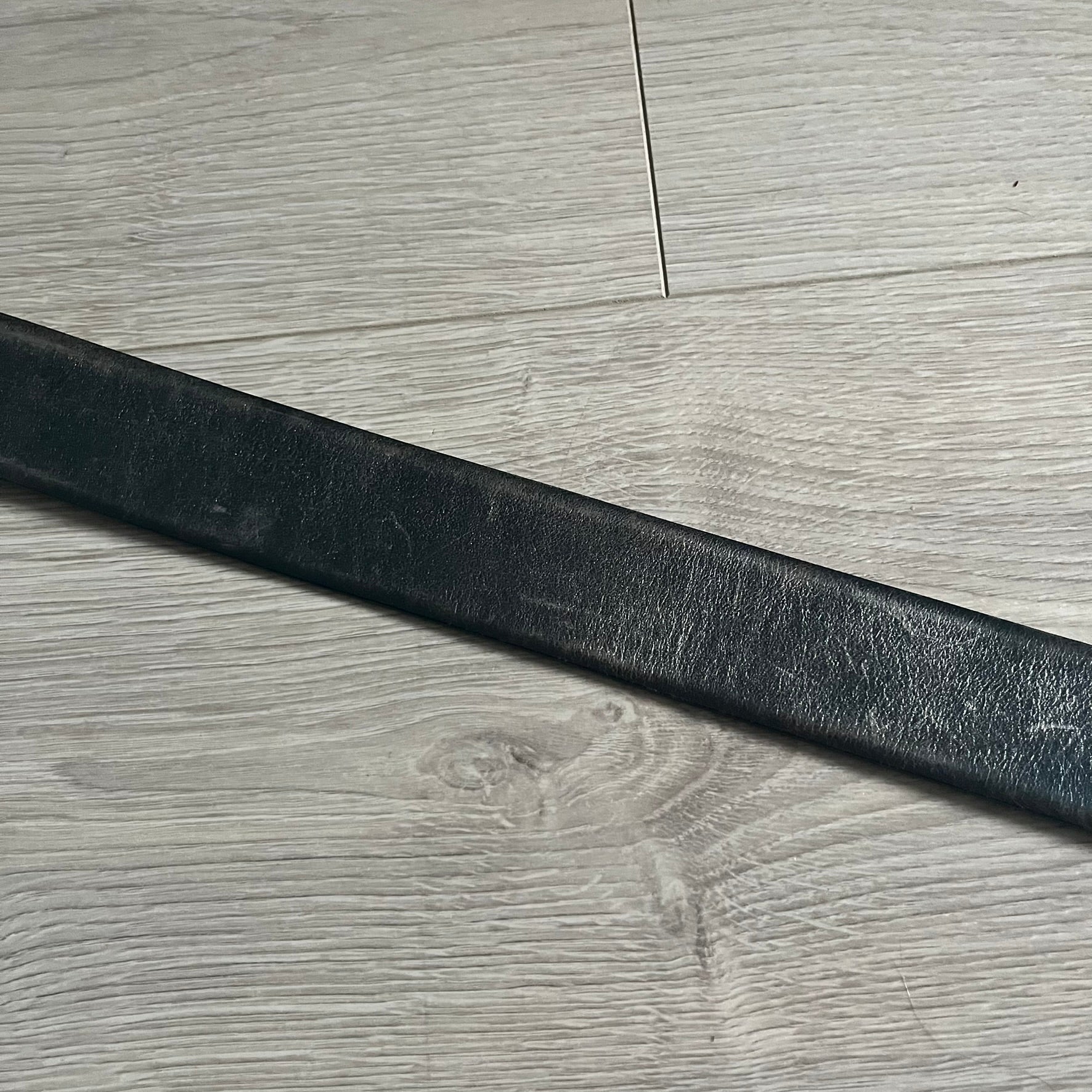 Dolce &amp; Gabbana Round Stamp Belt with a circular, wavy-edged buckle in a metallic finish. The buckle features a beige center with a bold black D&amp;G logo and “Dolce &amp; Gabbana” text beneath. Belt strap is glittery metallic blue with a black inner lining.
