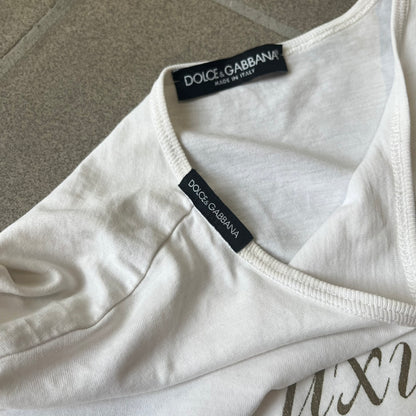 Dolce & Gabbana SS05 "Luxury Is a Dream!" White Tee features a clean white cotton design with dark gold handwritten-style text across the front reading “Luxury Is a Dream!”. The graphic uses a decorative quill-like font for a refined luxury aesthetic. Made in Italy, the tee includes two black Dolce & Gabbana tags, one at the neck and one on the collar.
