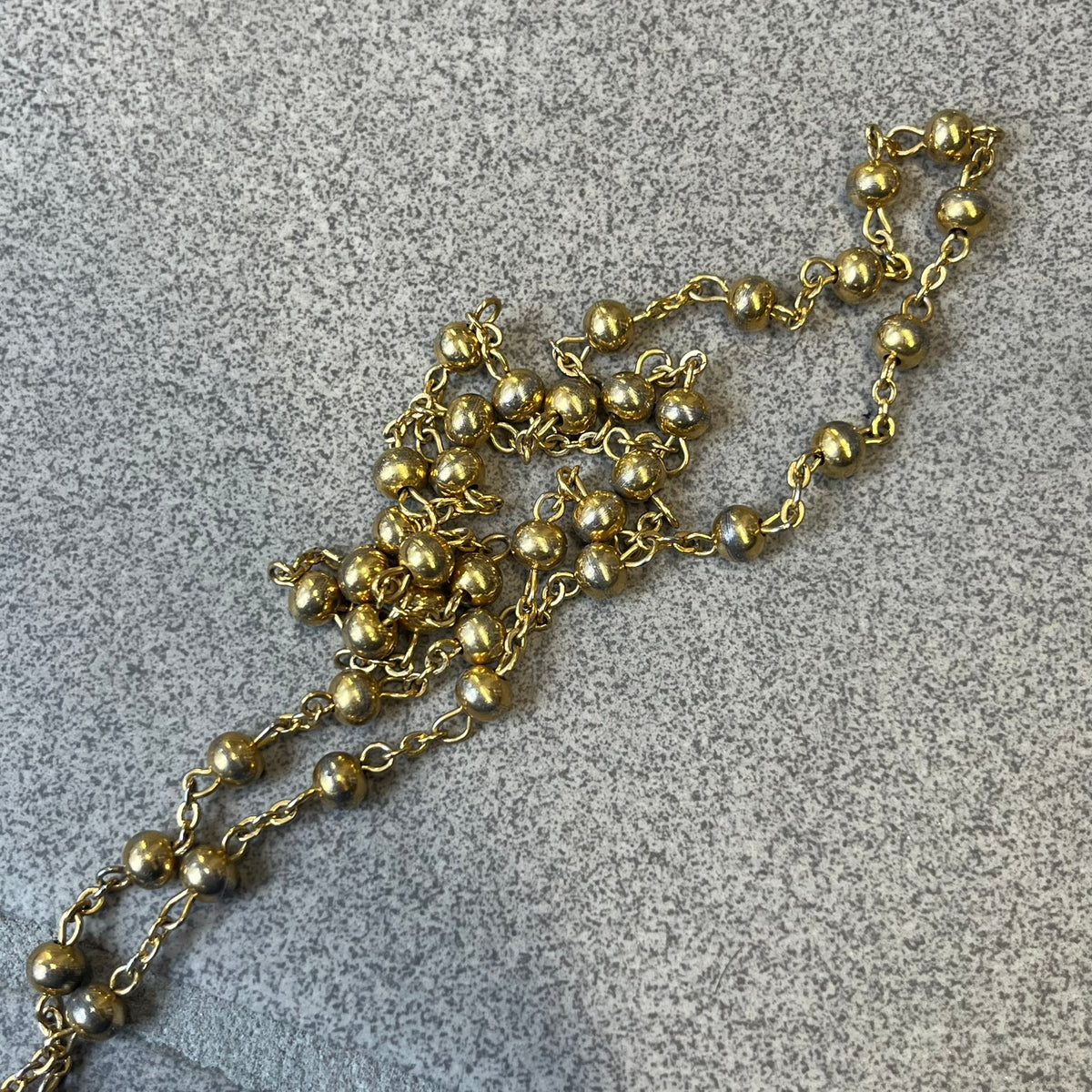 Dolce & Gabbana SS2003 Golden Cross Dog Tag Necklace features a curved-edge dog tag pendant with a cutout Latin cross in the center and engraved "Dolce & Gabbana" script text below it. It comes on a thin chain set with fixed beaded accents at regular intervals.