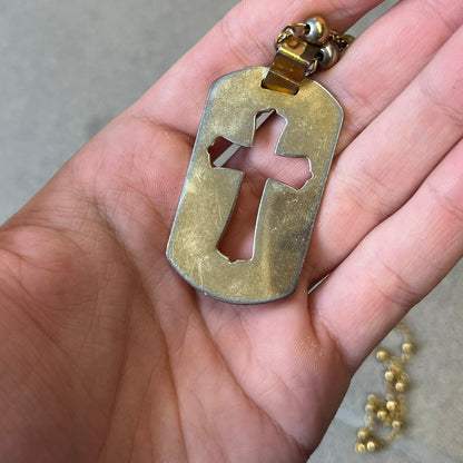 Dolce & Gabbana SS2003 Golden Cross Dog Tag Necklace features a curved-edge dog tag pendant with a cutout Latin cross in the center and engraved "Dolce & Gabbana" script text below it. It comes on a thin chain set with fixed beaded accents at regular intervals.