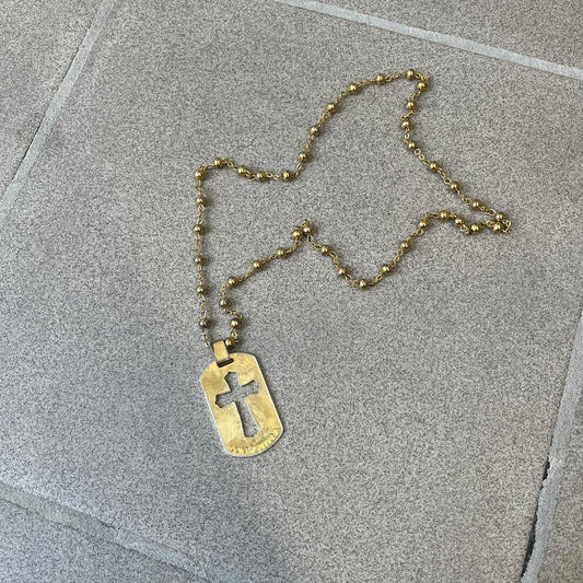 Dolce & Gabbana SS2003 Golden Cross Dog Tag Necklace features a curved-edge dog tag pendant with a cutout Latin cross in the center and engraved "Dolce & Gabbana" script text below it. It comes on a thin chain set with fixed beaded accents at regular intervals.