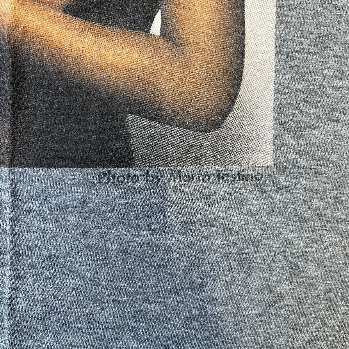 Dolce &amp; Gabbana SS2011 Naomi Campbell Grey Tee is a gray T-shirt with a photo of Naomi Campbell on the front, covering her chest with her hand, and small “Photo by Mario Testino” text below it. The upper back has “D&amp;G 3 L'Imperatrice” text. The shirt is constructed inside-out style, with the stitching visible along the sides.&nbsp;
