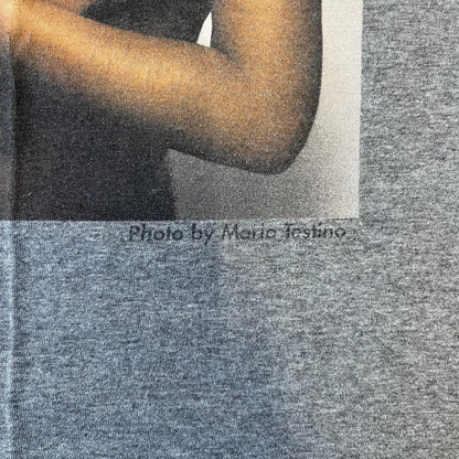 Dolce &amp; Gabbana SS2011 Naomi Campbell Grey Tee is a gray T-shirt with a photo of Naomi Campbell on the front, covering her chest with her hand, and small “Photo by Mario Testino” text below it. The upper back has “D&amp;G 3 L'Imperatrice” text. The shirt is constructed inside-out style, with the stitching visible along the sides.&nbsp;
