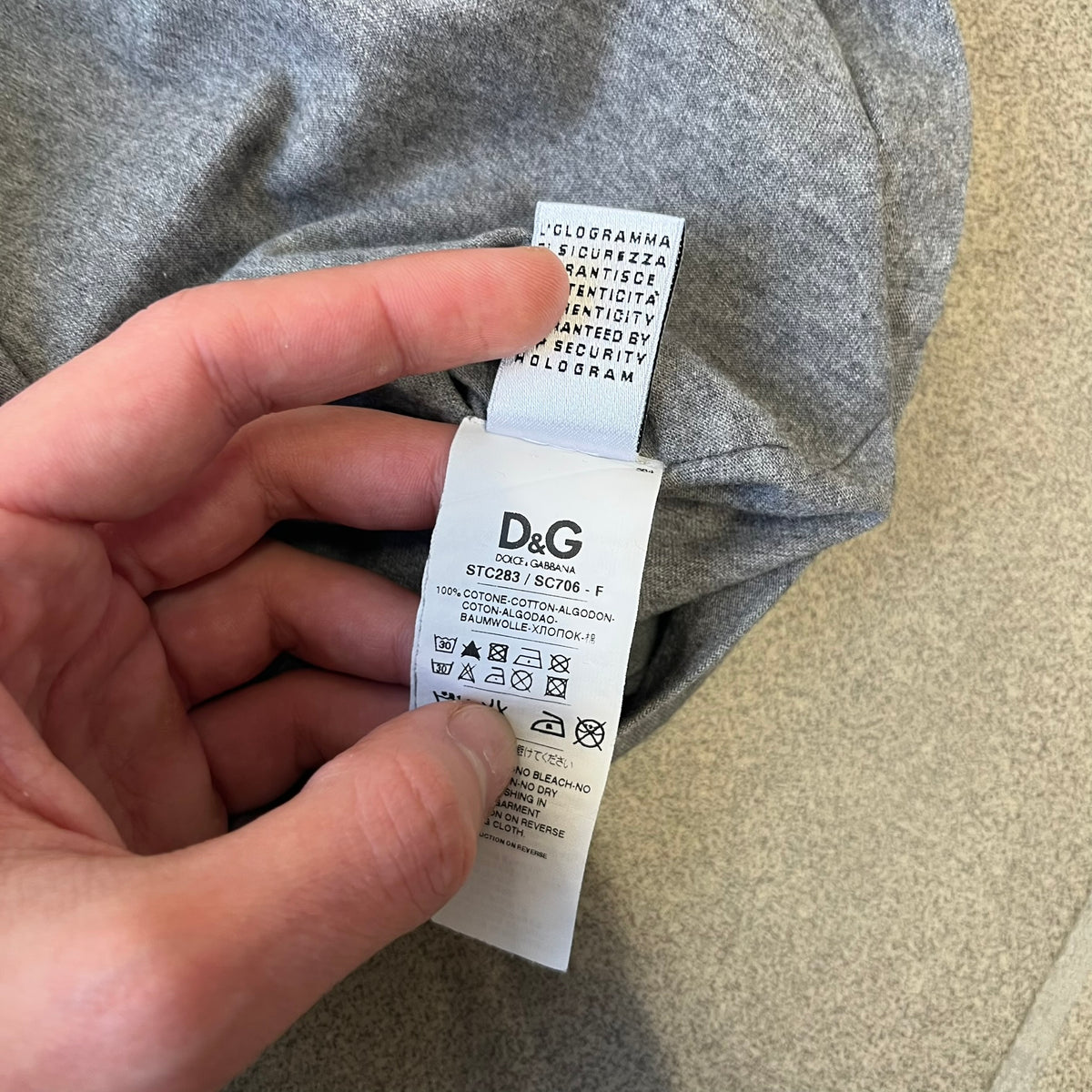 Dolce &amp; Gabbana SS2011 Naomi Campbell Grey Tee is a gray T-shirt with a photo of Naomi Campbell on the front, covering her chest with her hand, and small “Photo by Mario Testino” text below it. The upper back has “D&amp;G 3 L'Imperatrice” text. The shirt is constructed inside-out style, with the stitching visible along the sides.&nbsp;
