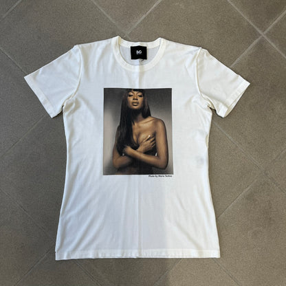 Dolce &amp; Gabbana SS2011 Naomi Campbell White Tee is a white T-shirt with a photo of Naomi Campbell on the front, covering her chest with her hand, and small “Photo by Mario Testino” text below it. The upper back has “D&amp;G 3 L'Imperatrice” text. The shirt is constructed inside-out style, with the stitching visible along the sides