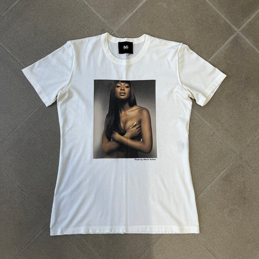 Dolce &amp; Gabbana SS2011 Naomi Campbell White Tee is a white T-shirt with a photo of Naomi Campbell on the front, covering her chest with her hand, and small “Photo by Mario Testino” text below it. The upper back has “D&amp;G 3 L'Imperatrice” text. The shirt is constructed inside-out style, with the stitching visible along the sides