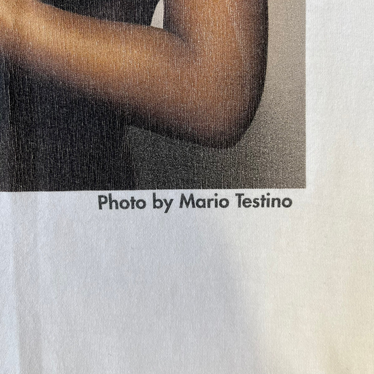 Dolce &amp; Gabbana SS2011 Naomi Campbell White Tee is a white T-shirt with a photo of Naomi Campbell on the front, covering her chest with her hand, and small “Photo by Mario Testino” text below it. The upper back has “D&amp;G 3 L'Imperatrice” text. The shirt is constructed inside-out style, with the stitching visible along the sides