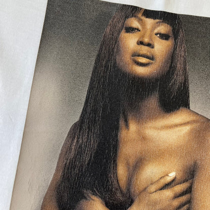 Dolce &amp; Gabbana SS2011 Naomi Campbell White Tee is a white T-shirt with a photo of Naomi Campbell on the front, covering her chest with her hand, and small “Photo by Mario Testino” text below it. The upper back has “D&amp;G 3 L'Imperatrice” text. The shirt is constructed inside-out style, with the stitching visible along the sides