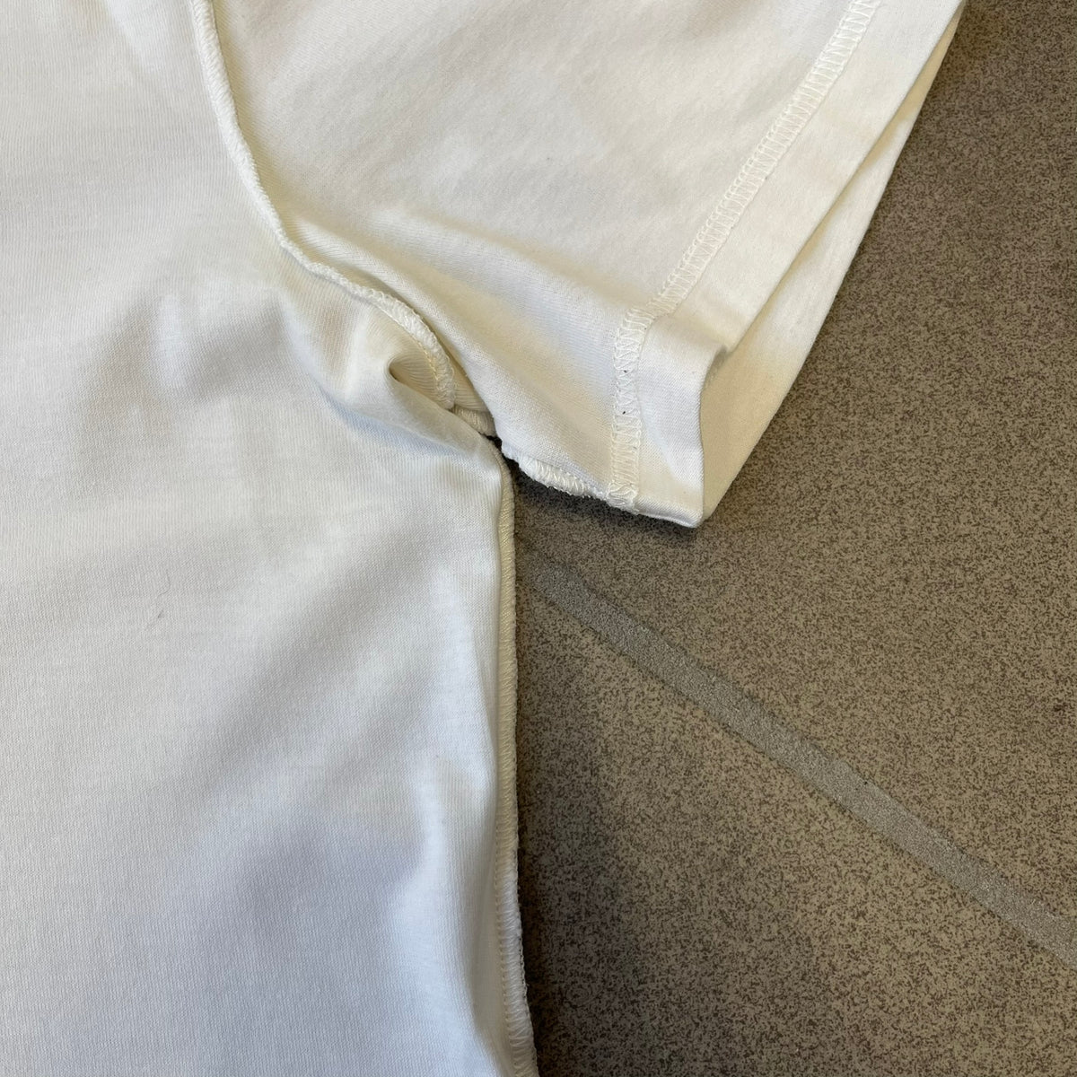 Dolce &amp; Gabbana SS2011 Naomi Campbell White Tee is a white T-shirt with a photo of Naomi Campbell on the front, covering her chest with her hand, and small “Photo by Mario Testino” text below it. The upper back has “D&amp;G 3 L'Imperatrice” text. The shirt is constructed inside-out style, with the stitching visible along the sides