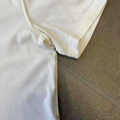 Dolce &amp; Gabbana SS2011 Naomi Campbell White Tee is a white T-shirt with a photo of Naomi Campbell on the front, covering her chest with her hand, and small “Photo by Mario Testino” text below it. The upper back has “D&amp;G 3 L'Imperatrice” text. The shirt is constructed inside-out style, with the stitching visible along the sides