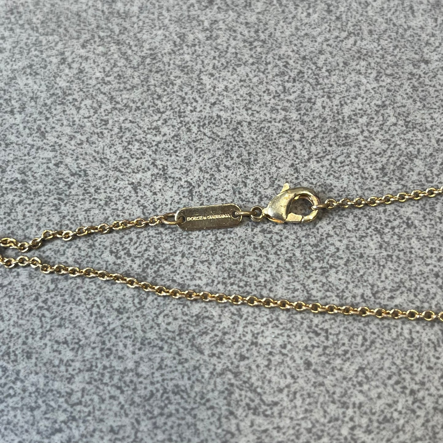 Dolce &amp; Gabbana SS25 Gold Cross Necklace features a gold-tone brass chain with a detailed 3D cross pendant depicting Jesus. A Dolce &amp; Gabbana plaque with “Made in Italy” text is positioned near the clasp. Comes with the original black box and certificate card.