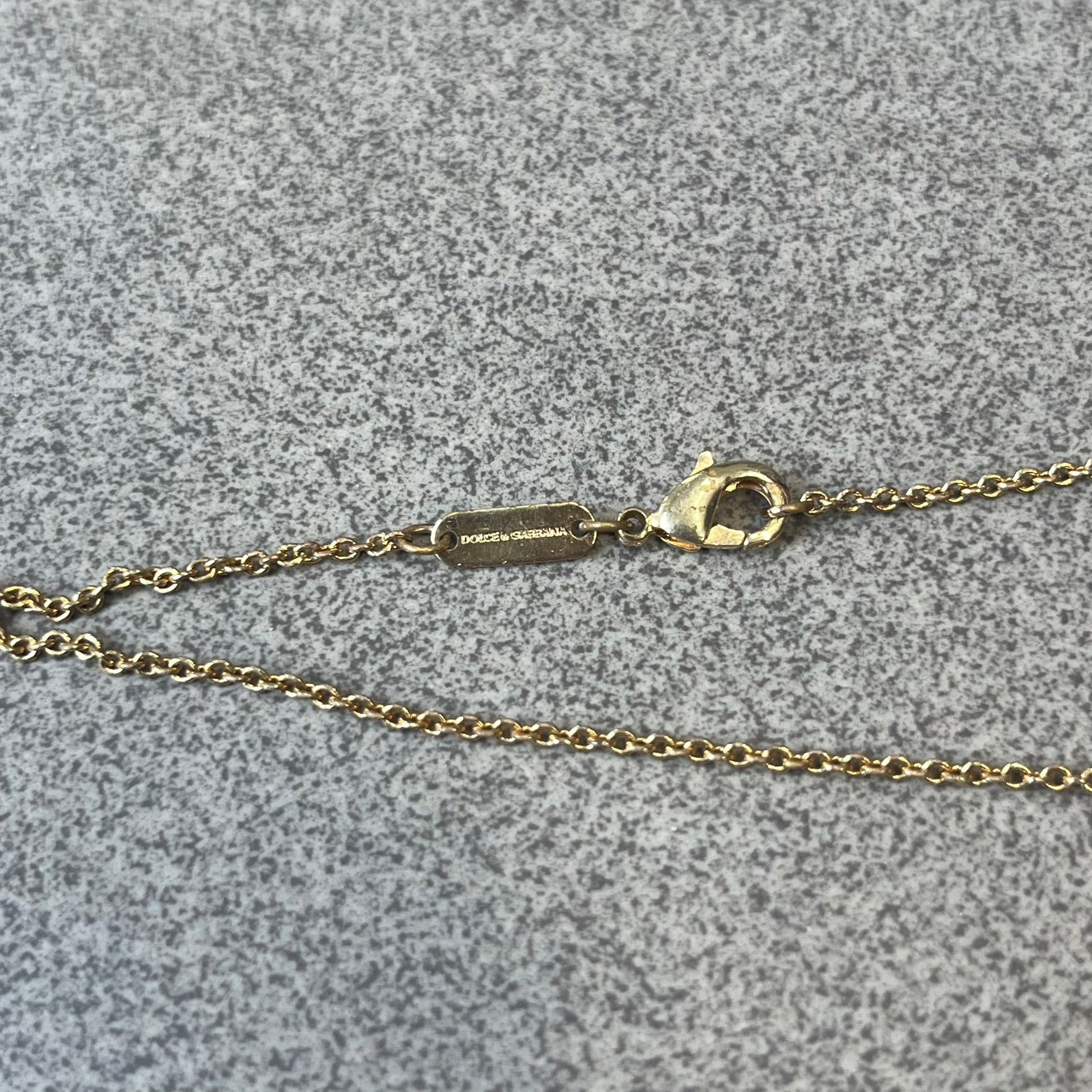Dolce &amp; Gabbana SS25 Gold Cross Necklace features a gold-tone brass chain with a detailed 3D cross pendant depicting Jesus. A Dolce &amp; Gabbana plaque with “Made in Italy” text is positioned near the clasp. Comes with the original black box and certificate card.