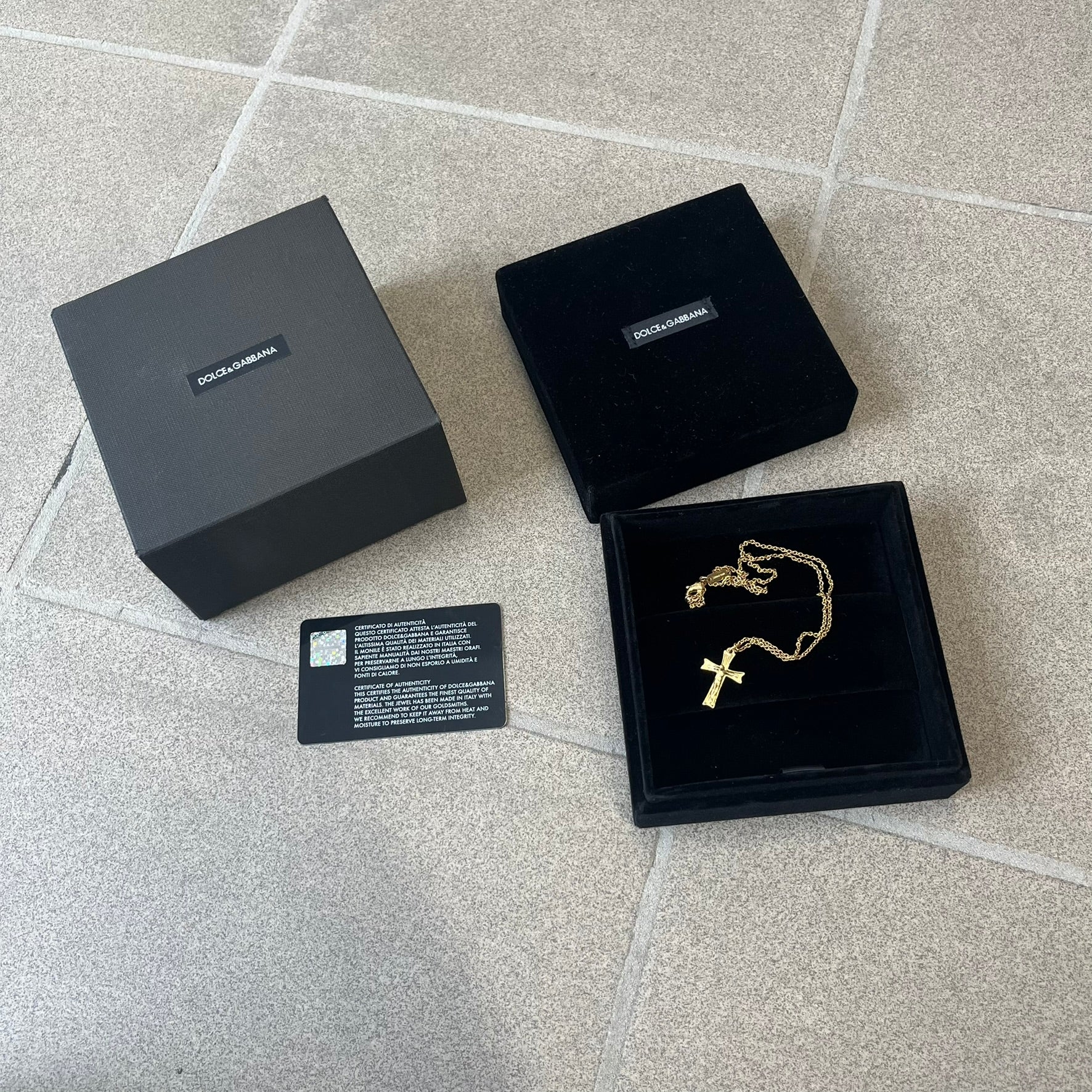 Dolce &amp; Gabbana SS25 Gold Cross Necklace features a gold-tone brass chain with a detailed 3D cross pendant depicting Jesus. A Dolce &amp; Gabbana plaque with “Made in Italy” text is positioned near the clasp. Comes with the original black box and certificate card.