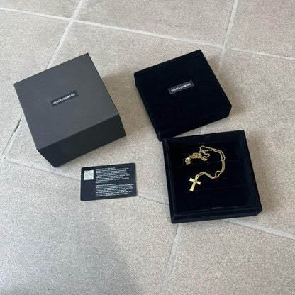 Dolce &amp; Gabbana SS25 Gold Cross Necklace features a gold-tone brass chain with a detailed 3D cross pendant depicting Jesus. A Dolce &amp; Gabbana plaque with “Made in Italy” text is positioned near the clasp. Comes with the original black box and certificate card.