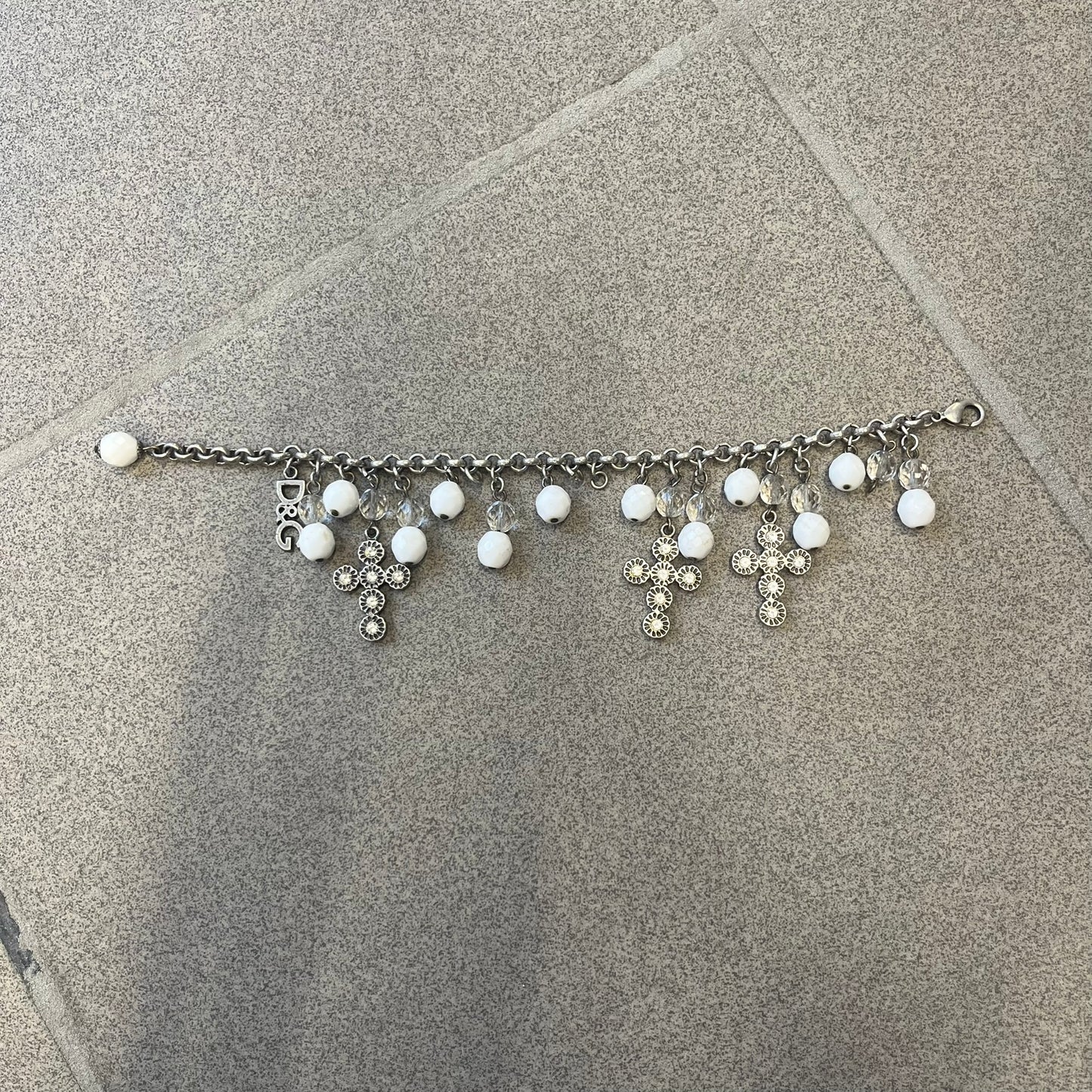 Dolce &amp; Gabbana Silver Charm Cross DJ0253 Bracelet features a silver-tone chain bracelet with white bead charms, three cross-shaped charms made from circular elements, and a D&amp;G logo charm. The bracelet has a silver-tone metal construction.&nbsp;