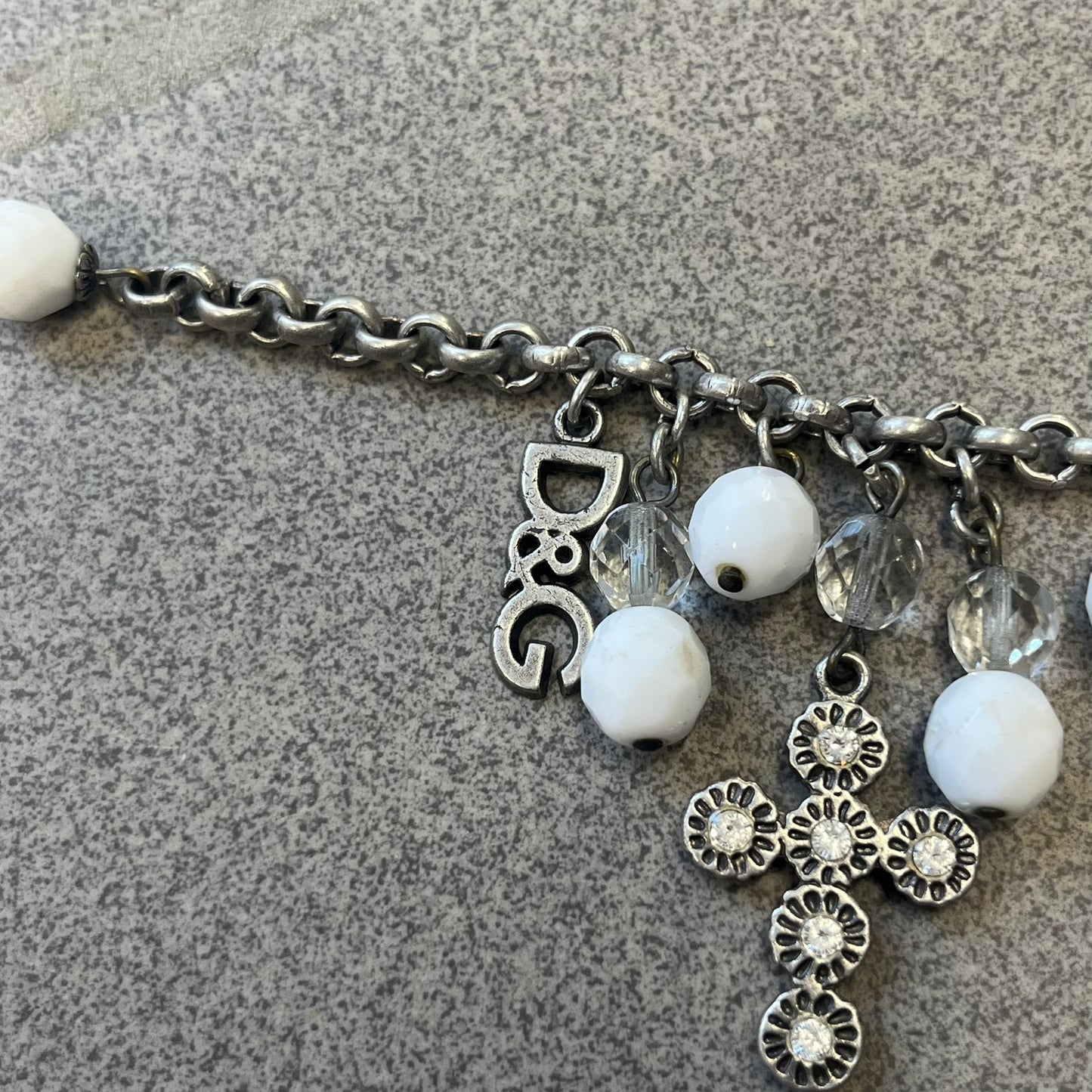 Dolce &amp; Gabbana Silver Charm Cross DJ0253 Bracelet features a silver-tone chain bracelet with white bead charms, three cross-shaped charms made from circular elements, and a D&amp;G logo charm. The bracelet has a silver-tone metal construction.&nbsp;