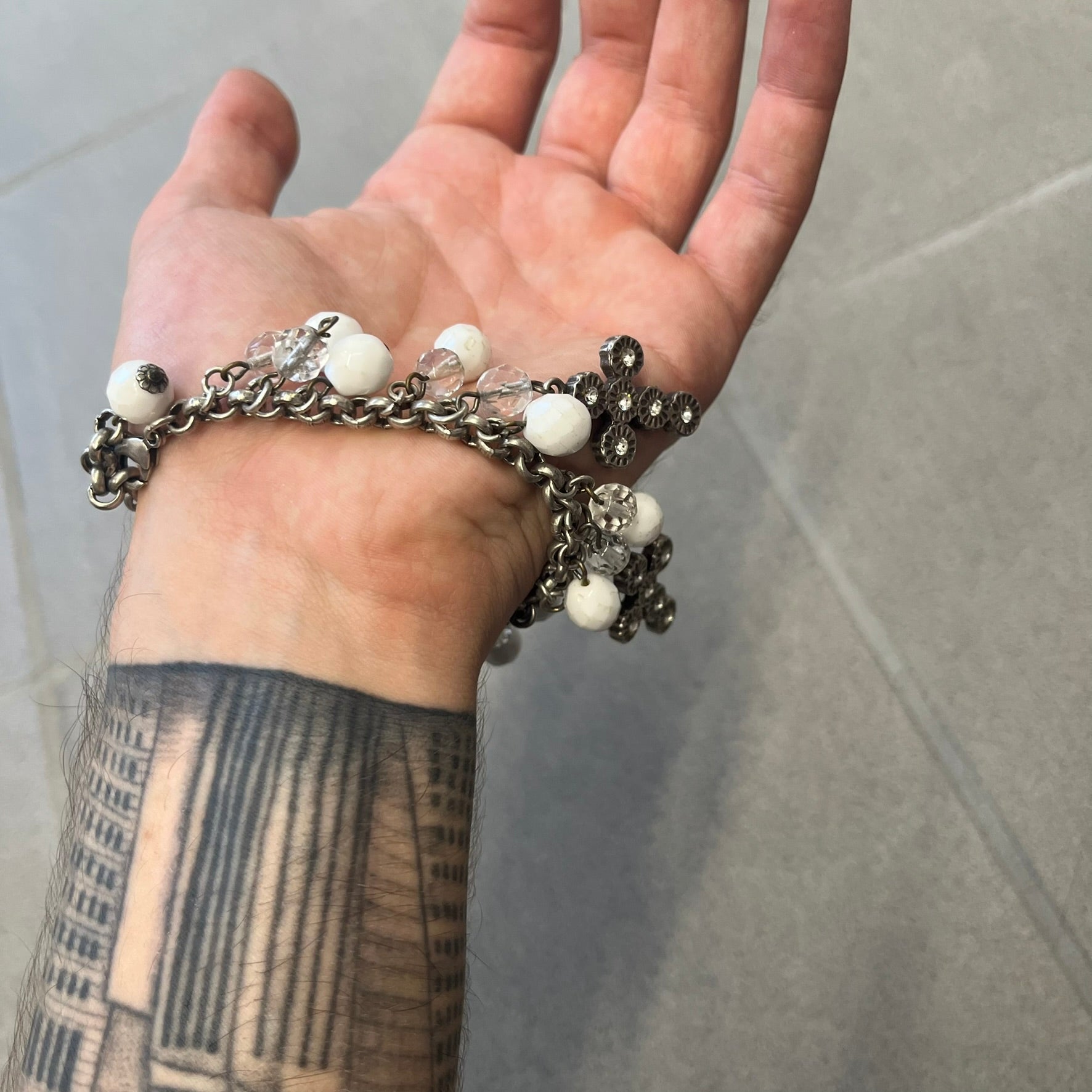 Dolce &amp; Gabbana Silver Charm Cross DJ0253 Bracelet features a silver-tone chain bracelet with white bead charms, three cross-shaped charms made from circular elements, and a D&amp;G logo charm. The bracelet has a silver-tone metal construction.&nbsp;
