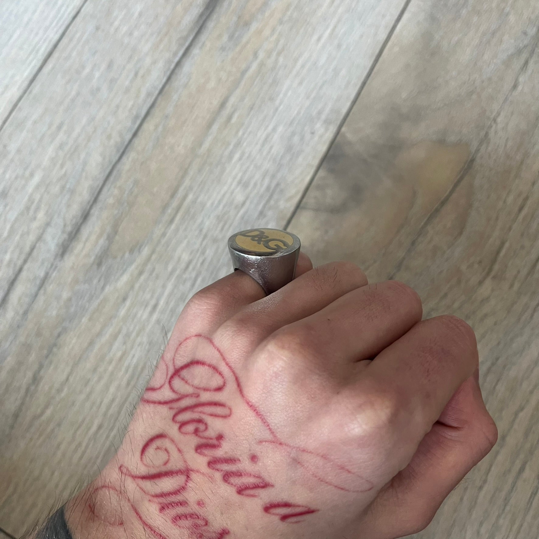 The Dolce &amp; Gabbana Silver Logo Signet Ring is a silver-tone metal signet ring with a thick, substantial design. The top features a beige background with the D&amp;G logo in silver tone, outlined in silver. The signet is large and solid.