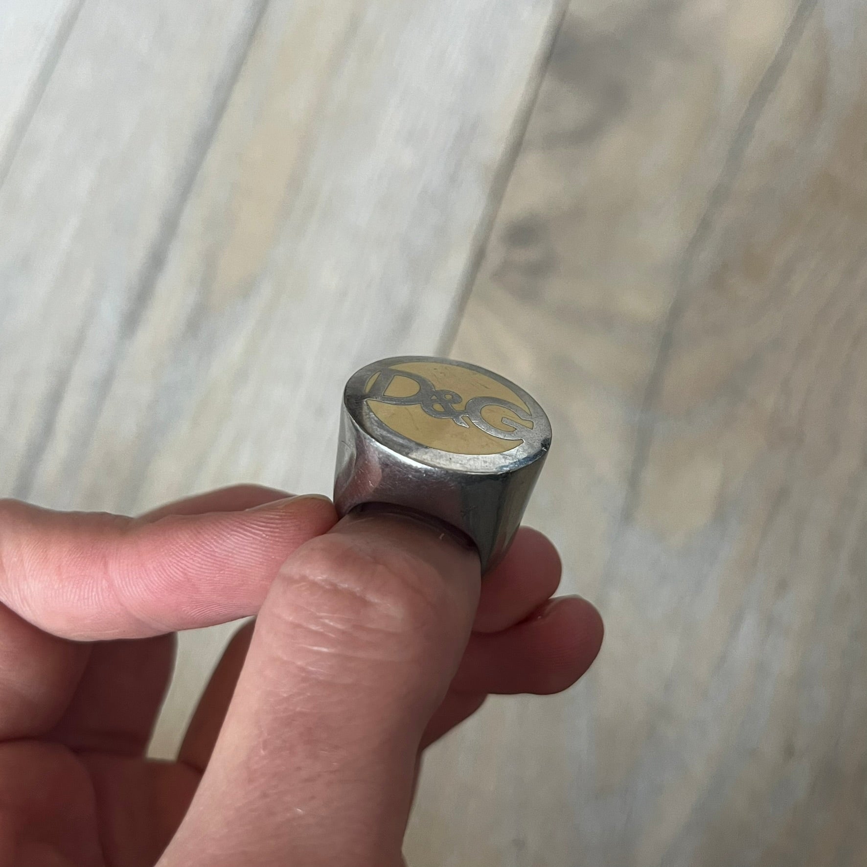 The Dolce &amp; Gabbana Silver Logo Signet Ring is a silver-tone metal signet ring with a thick, substantial design. The top features a beige background with the D&amp;G logo in silver tone, outlined in silver. The signet is large and solid.