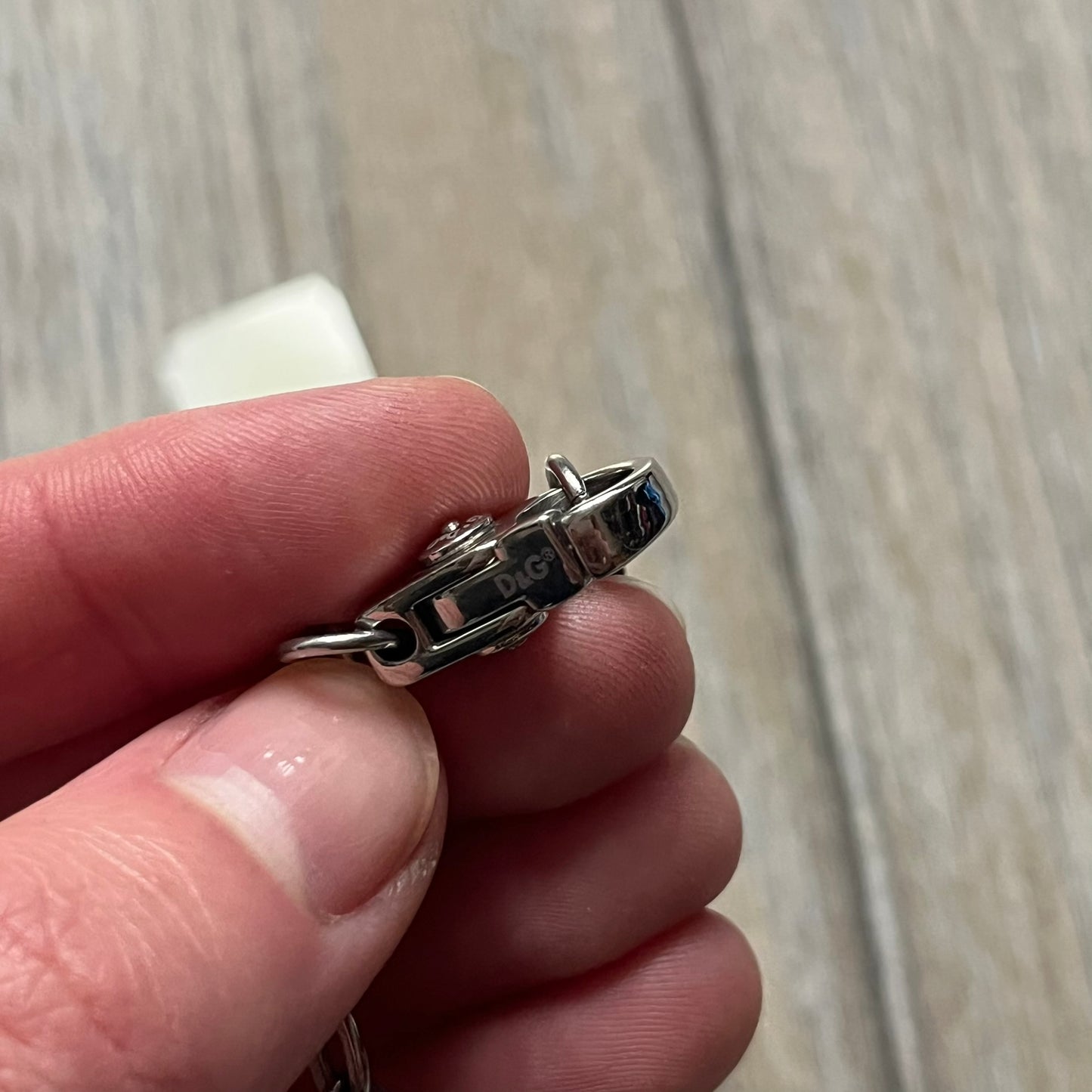 The Dolce & Gabbana Star Dog Tag Necklace (DJ0889) is a heavy stainless steel necklace featuring a thick, oversized dog tag pendant. The front of the pendant has a raised black star mounted on a silver-tone circular base, with open cutout sections between the star and the circle. A raised D&G logo is positioned at the lower front of the dog tag. The necklace is finished with a lobster clasp and has a solid, weighty construction throughout.