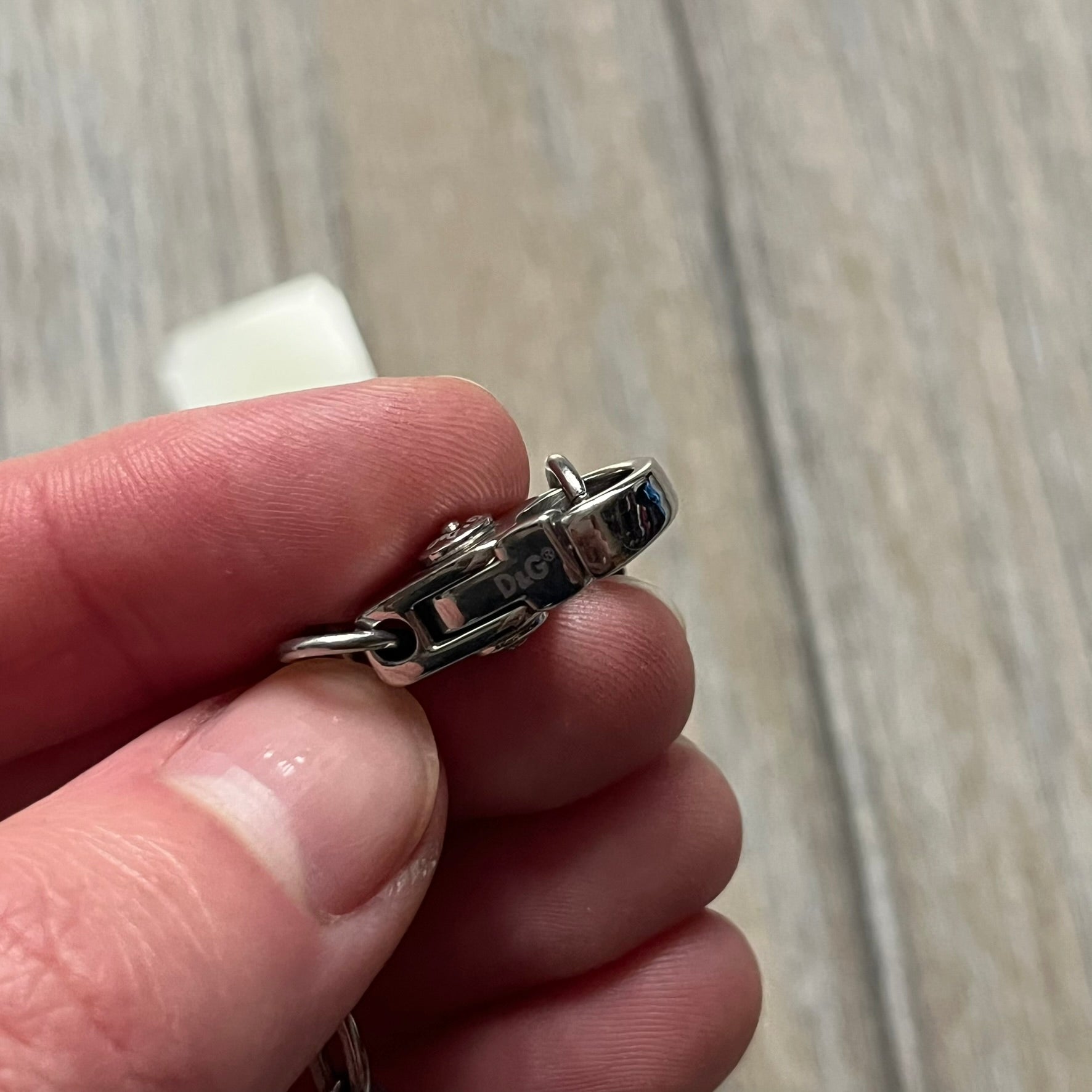 The Dolce & Gabbana Star Dog Tag Necklace (DJ0889) is a heavy stainless steel necklace featuring a thick, oversized dog tag pendant. The front of the pendant has a raised black star mounted on a silver-tone circular base, with open cutout sections between the star and the circle. A raised D&G logo is positioned at the lower front of the dog tag. The necklace is finished with a lobster clasp and has a solid, weighty construction throughout.