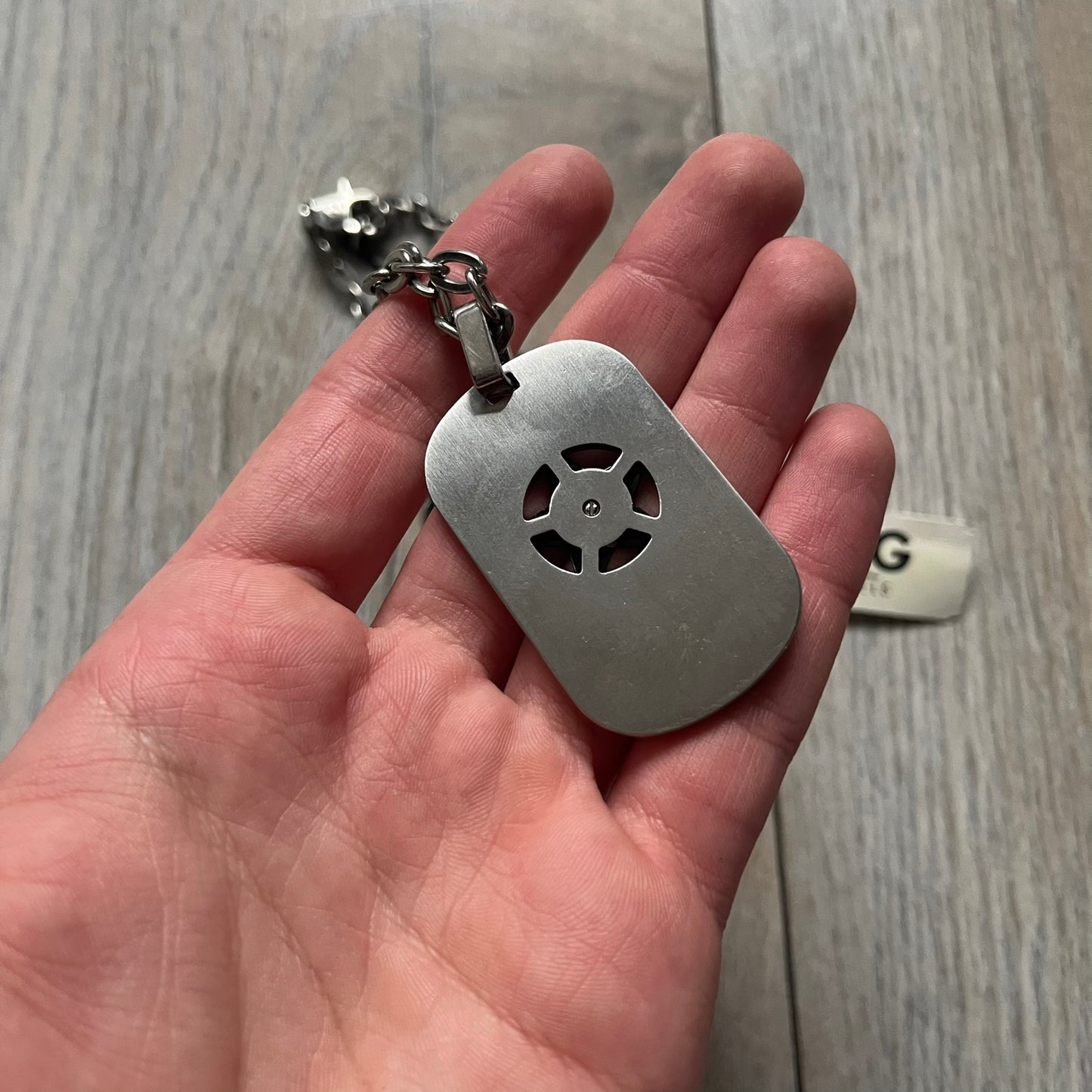 The Dolce & Gabbana Star Dog Tag Necklace (DJ0889) is a heavy stainless steel necklace featuring a thick, oversized dog tag pendant. The front of the pendant has a raised black star mounted on a silver-tone circular base, with open cutout sections between the star and the circle. A raised D&G logo is positioned at the lower front of the dog tag. The necklace is finished with a lobster clasp and has a solid, weighty construction throughout.