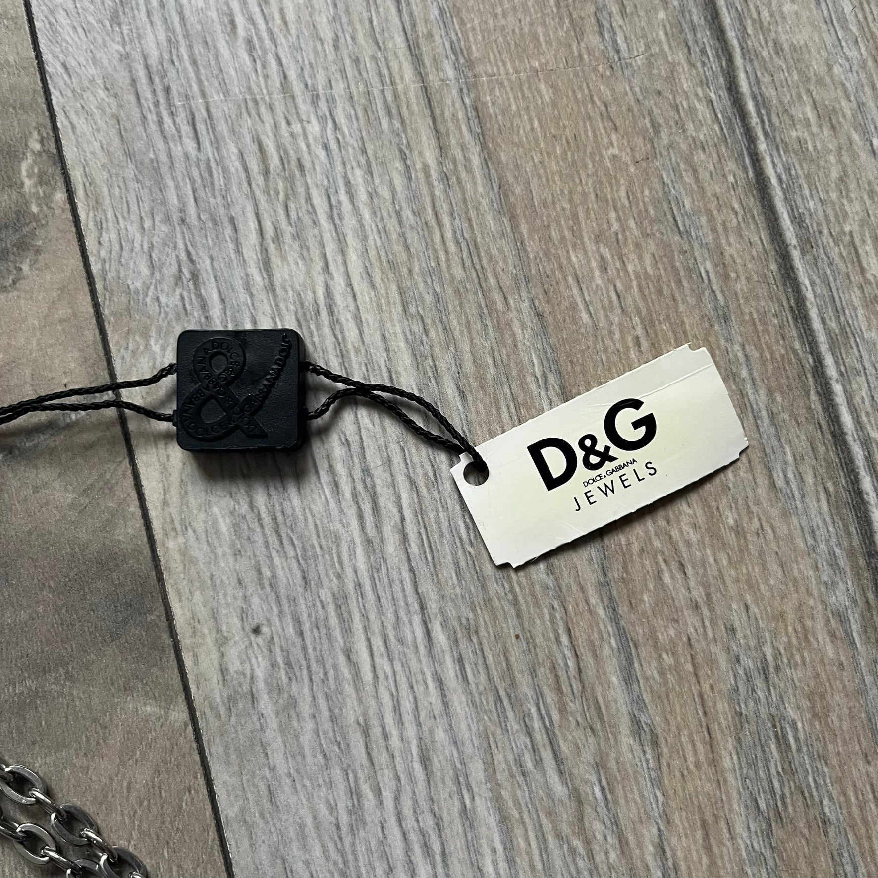 The Dolce & Gabbana Star Dog Tag Necklace (DJ0889) is a heavy stainless steel necklace featuring a thick, oversized dog tag pendant. The front of the pendant has a raised black star mounted on a silver-tone circular base, with open cutout sections between the star and the circle. A raised D&G logo is positioned at the lower front of the dog tag. The necklace is finished with a lobster clasp and has a solid, weighty construction throughout.