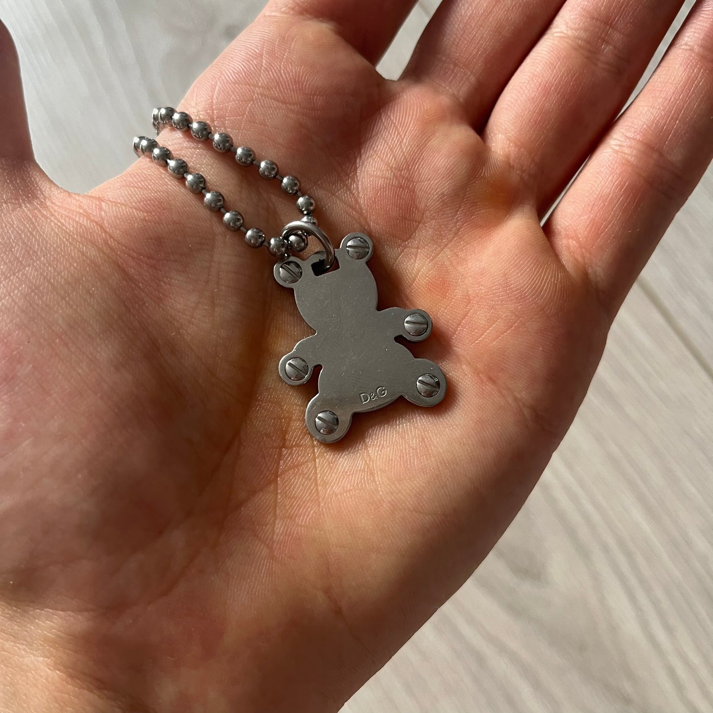 Silver pendant on a chain held in a hand against a neutral background