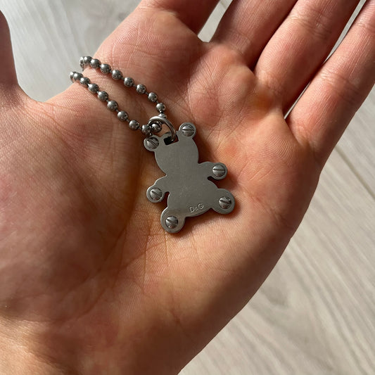 Silver pendant on a chain held in a hand against a neutral background