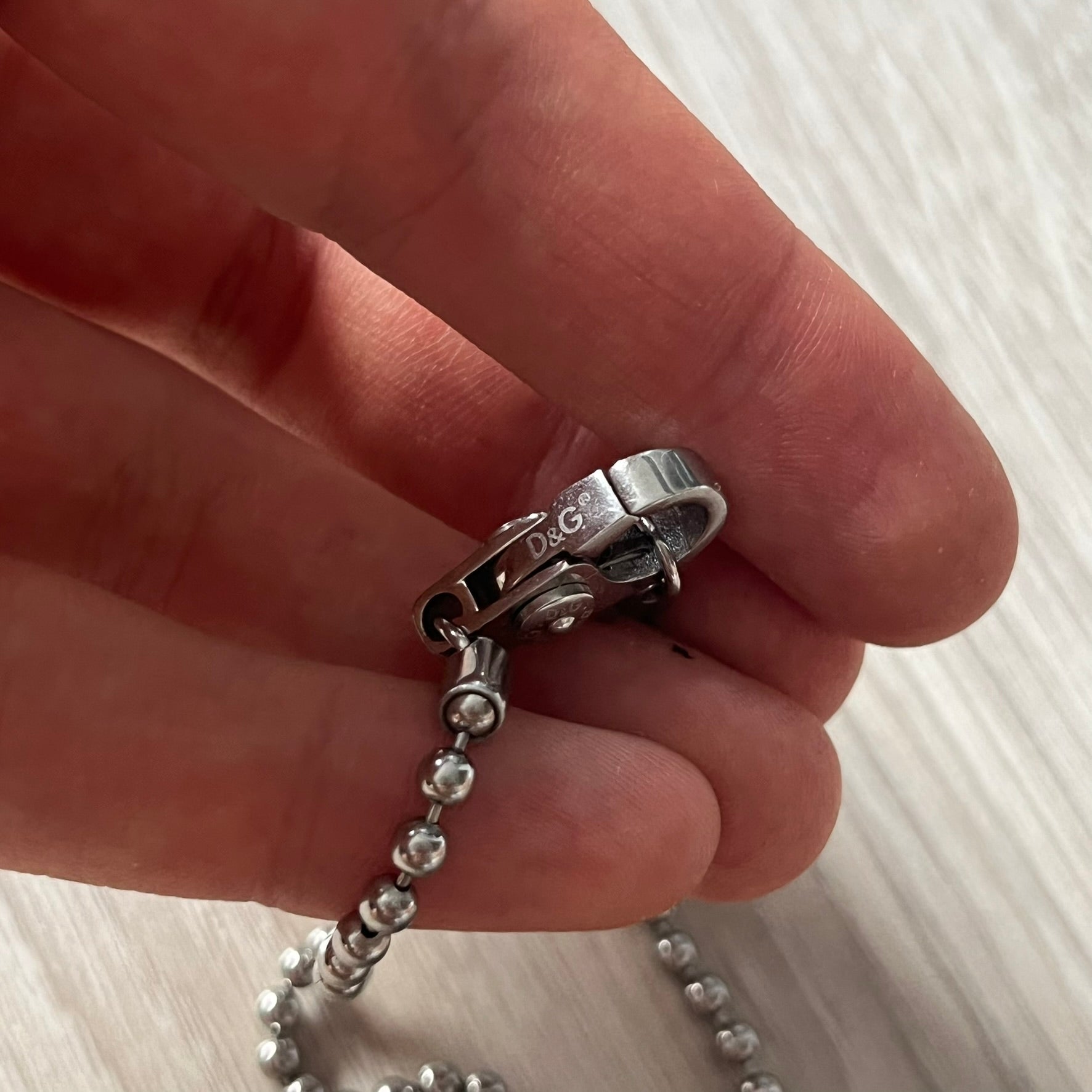 Close-up of a hand holding a silver chain with a clasp.