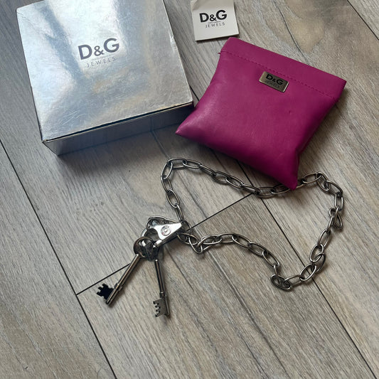 Dolce & Gabbana Two Keys Necklace is a stainless steel necklace featuring a paperclip chain design. At the center, it has a large lobster clasp holding two D&G logo-tagged keys, one with a circular top and the other with a square top. The clasp is engraved in multiple places, and the necklace comes with the original box and dust bag.