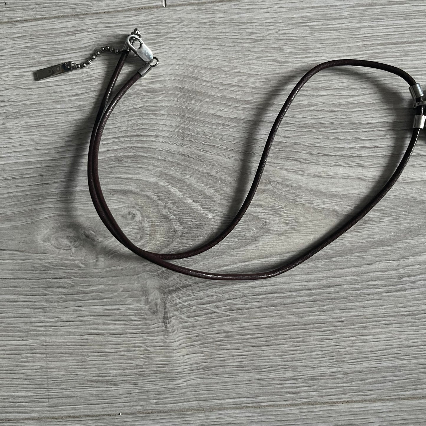 Dolce &amp; Gabbana double dog tag necklace featuring two layered pendants: a United Kingdom flag tag underneath and a silver-tone tag on top with a cut-out D&amp;G logo revealing the tricolor tag beneath. Designed with brown leather-ish string.