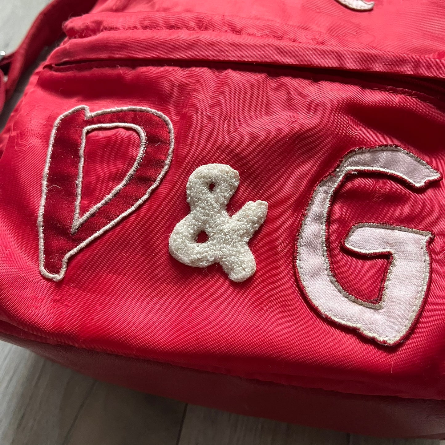 The Dolce & Gabbana "We Are D&G" Red Backpack is crafted from durable red nylon with metal hardware and features a graffiti-inspired "We Are D&G" logo embroidered on the front. It has a top zip closure, exterior zip pocket, padded back panel, and adjustable shoulder straps with canvas and faux leather details. The backpack also includes a top handle, rear identification label holder, and is made in Italy.