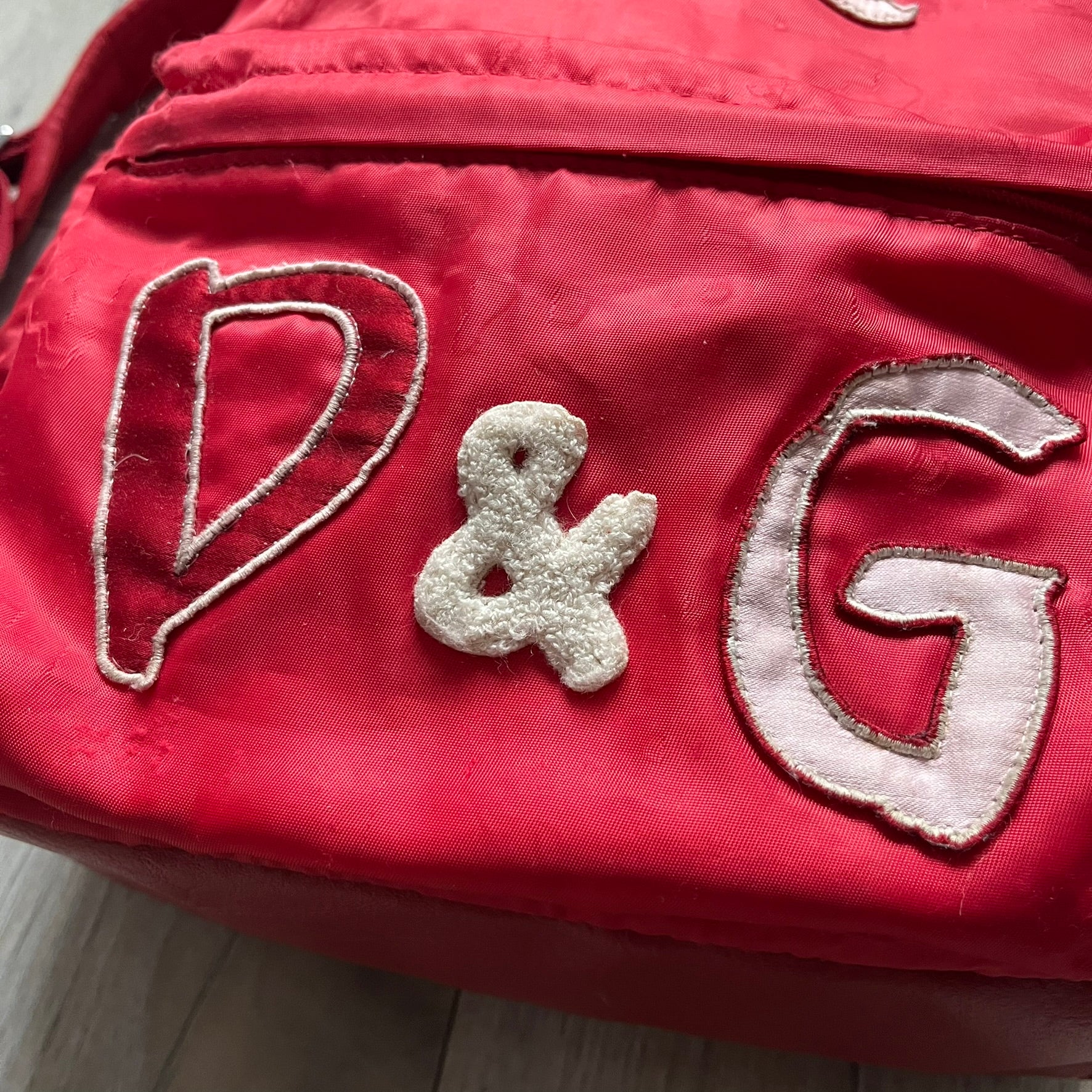 The Dolce & Gabbana "We Are D&G" Red Backpack is crafted from durable red nylon with metal hardware and features a graffiti-inspired "We Are D&G" logo embroidered on the front. It has a top zip closure, exterior zip pocket, padded back panel, and adjustable shoulder straps with canvas and faux leather details. The backpack also includes a top handle, rear identification label holder, and is made in Italy.