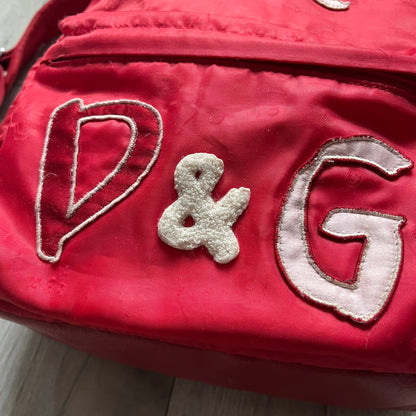 The Dolce & Gabbana "We Are D&G" Red Backpack is crafted from durable red nylon with metal hardware and features a graffiti-inspired "We Are D&G" logo embroidered on the front. It has a top zip closure, exterior zip pocket, padded back panel, and adjustable shoulder straps with canvas and faux leather details. The backpack also includes a top handle, rear identification label holder, and is made in Italy.