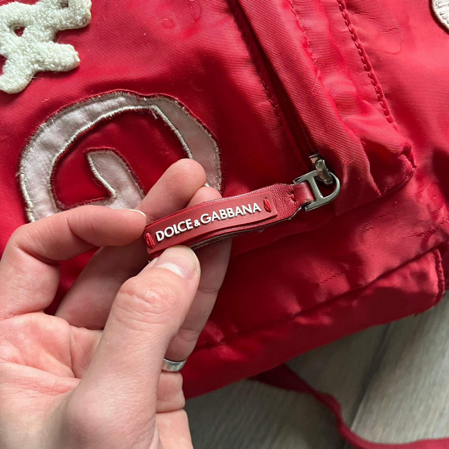 The Dolce & Gabbana "We Are D&G" Red Backpack is crafted from durable red nylon with metal hardware and features a graffiti-inspired "We Are D&G" logo embroidered on the front. It has a top zip closure, exterior zip pocket, padded back panel, and adjustable shoulder straps with canvas and faux leather details. The backpack also includes a top handle, rear identification label holder, and is made in Italy.