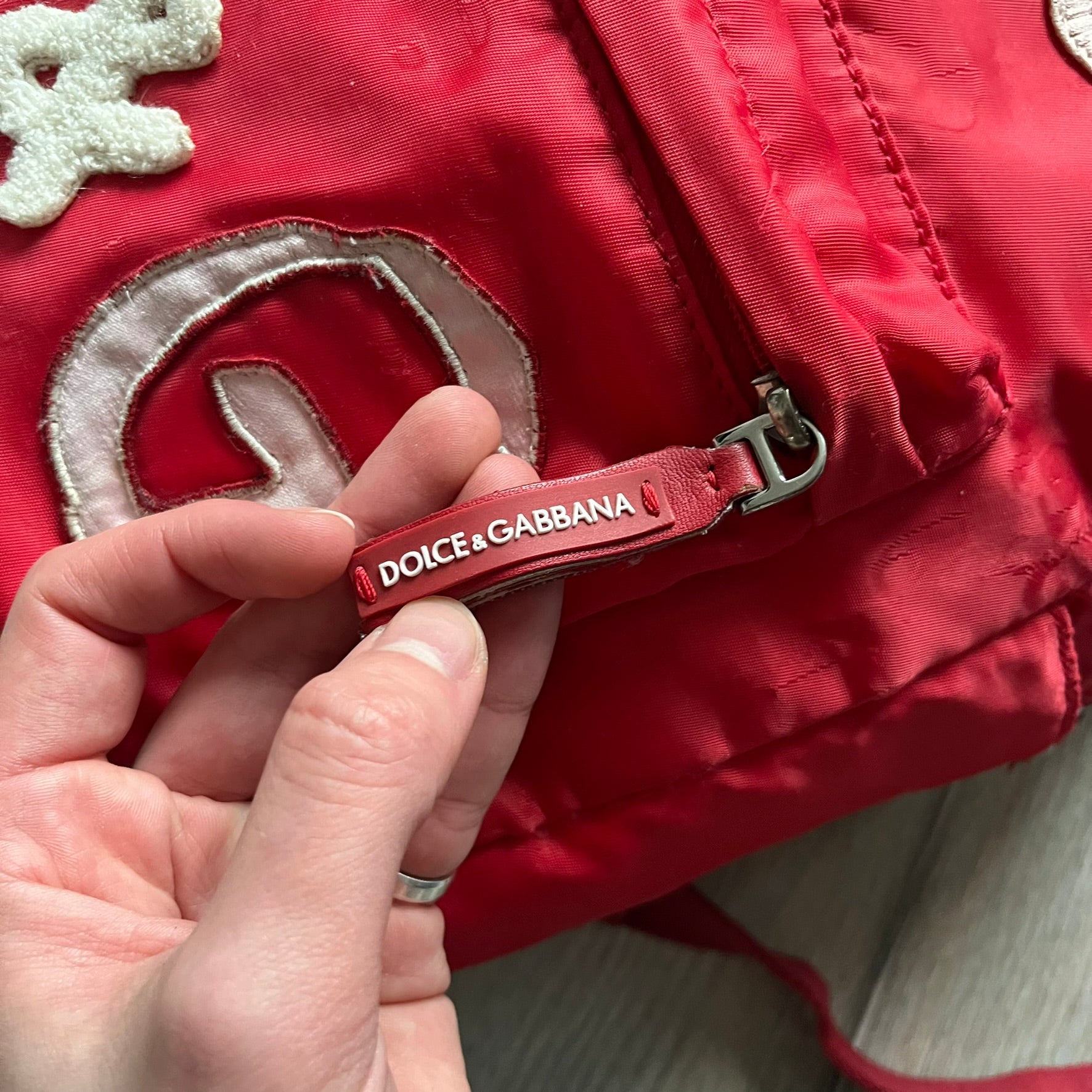 The Dolce & Gabbana "We Are D&G" Red Backpack is crafted from durable red nylon with metal hardware and features a graffiti-inspired "We Are D&G" logo embroidered on the front. It has a top zip closure, exterior zip pocket, padded back panel, and adjustable shoulder straps with canvas and faux leather details. The backpack also includes a top handle, rear identification label holder, and is made in Italy.