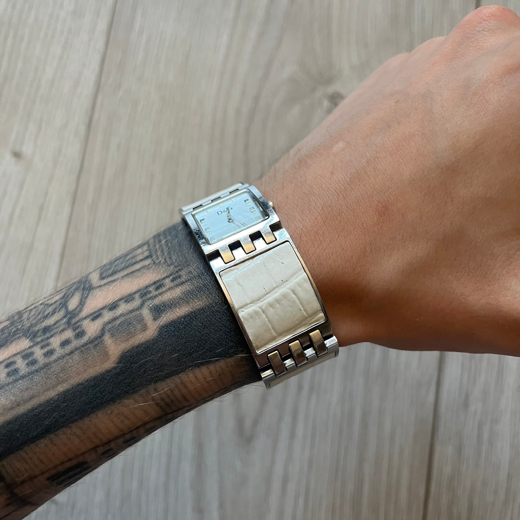 Dolce &amp; Gabbana white analog watch with a silver bracelet featuring white leather-like panels. The case seamlessly aligns with the width of the bracelet for a sleek, integrated look. A refined statement piece blending luxury design with modern elegance.