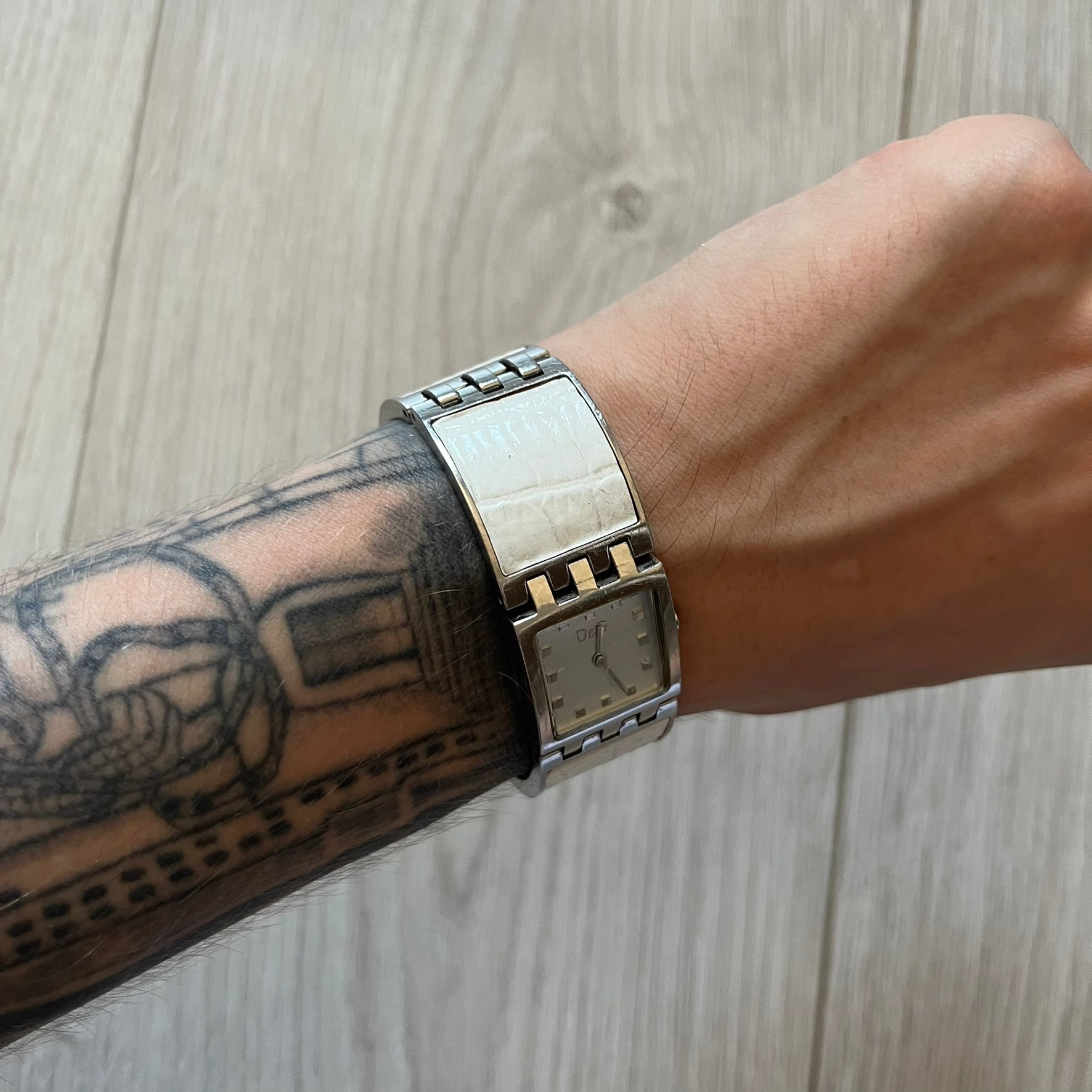 Dolce &amp; Gabbana white analog watch with a silver bracelet featuring white leather-like panels. The case seamlessly aligns with the width of the bracelet for a sleek, integrated look. A refined statement piece blending luxury design with modern elegance.