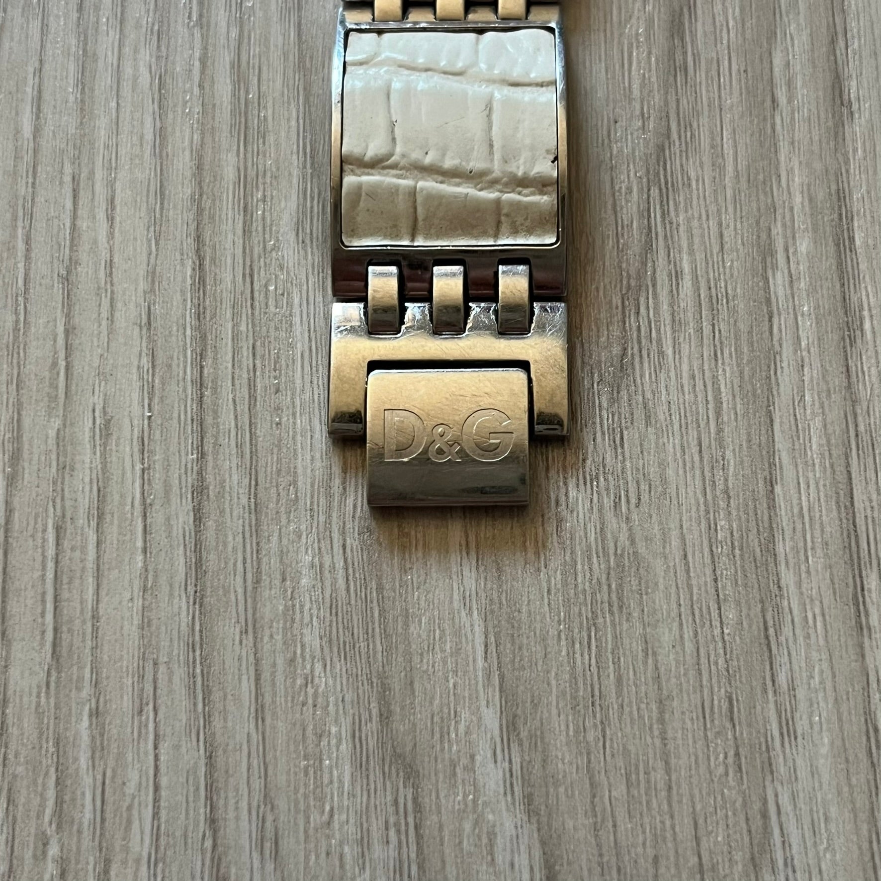 Dolce &amp; Gabbana white analog watch with a silver bracelet featuring white leather-like panels. The case seamlessly aligns with the width of the bracelet for a sleek, integrated look. A refined statement piece blending luxury design with modern elegance.
